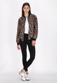 Jachetă bomber cu imprimeu leopard, din material maro și negru, cu fermoar în față, manșete cu nervuri, asortată cu colanți negri și adidași albi.