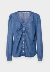 Blouse en denim à manches longues, col en V, fronces élastiques à l'avant et fermeture à boutons au centre. Couleur bleu clair, texture lisse.