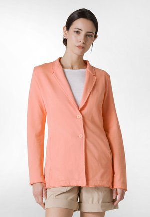 ferskenfarvet blazer med to knapper, slået krave og lange ærmer. Båret over en hvid top og parret med khaki shorts. Glat tekstur.