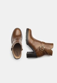 Bruine leren enkellaarzen met een ronde neus, een zijrits en een decoratieve metalen ringaccent. Chunky hak en een getextureerde rubberen zool.