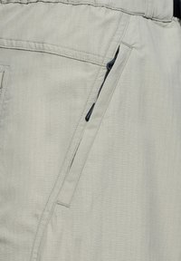 Ljust grå, texturerad tygshorts med en dragkedjeförsedd sidoficka och dekorsöm, utformad för hållbarhet och funktionalitet.