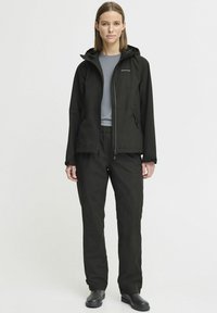 Black waterproof jacket with a zip front, adjustable hood, and two side pockets, paired with black elastic-waist pants and black boots.