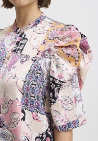 Blusa colorata caratterizzata da un mix di motivi floreali e geometrici. Realizzata in tessuto leggero con maniche a sbuffo e scollatura a bottoni.