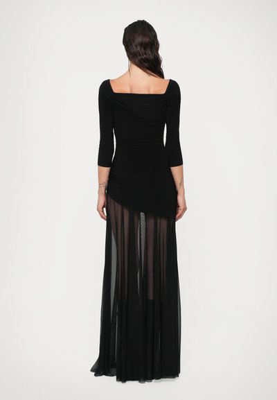 Rochie neagră cu un bust ajustat, cu decolteu pătrat și mâneci tridimensionale. Fusta este stratificată, realizată dintr-un material transparent, creând un efect fluid.