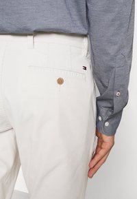 Pantalones de pana blancos con un bolsillo trasero y un botón marrón, combinados con una camisa de botones azul con una textura sutil.