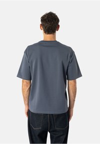 Szara koszulka z krótkim rękawem o luźnym kroju i okrągłym dekoltem, wykonana z miękkiego materiału. Noszona z ciemnymi dżinsami.