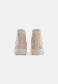 Vaaleanbeige korkeavartiset lenkkitossut, joissa on tekstuuripintainen kangas ja sileät nahkaosat, sekä valkoinen kumipohja. Logo-kuvio näkyy sivuilla.