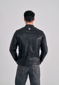 Černá kožená bunda s jednoduchým designem, s límcem na stojáka a viditelným prošíváním. Na zadní části límce je umístěna logo visačka.