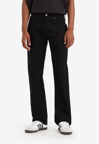 Zwarte denim jeans met een rechteloze pasvorm, voorzien van voorkpassen, een knoopsluiting en zilverkleurige hardware. G gedragen met witte sneakers.