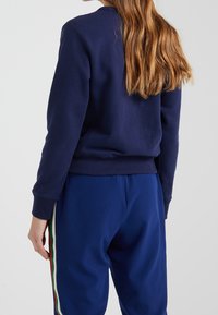 Sweatshirt bleu marine à col rond, avec des poignets et un ourlet côtelés ; associé à un pantalon de survêtement assorti avec des rayures latérales multicolores.