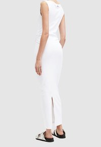 Weißes ärmelloses Kleid aus glattem Material, mit seitlichem Raffung und Rückenschlitz. Kombiniert mit flachen Sandalen.