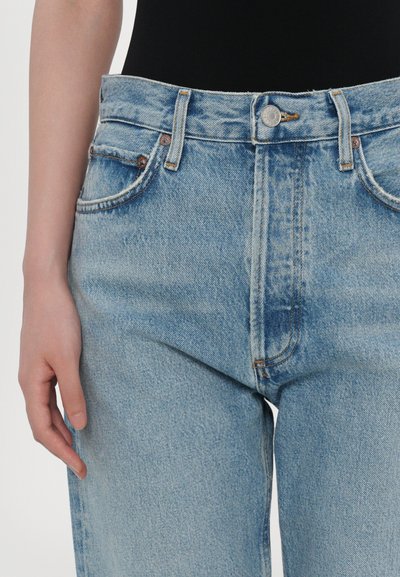 Τα ανοιχτό μπλε τζιν με ψηλή μέση, σχεδίαση με πέντε τσέπες, χρυστό ράψιμο και μεταλλικό κουμπί. Ομαλή υφή, ελαφρώς άνετη εφαρμογή.