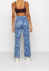 Pantalon cargo à motifs bleus avec dessins graphiques, doté d'une taille à cordon et de poches. Porté avec un haut court foncé.