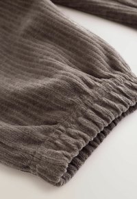 Brun ribbad tygärm med elastisk mudd, som visar mjuk textur och veckad detalj på vit bakgrund.