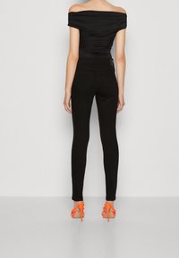 Černý top bez ramínek s zřasenou texturou v kombinaci s úzkými černými džíny a oranžovými sandály na vysokém podpatku, které dodávají živý akcent.