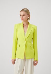 Blazer verde lime cu rever în notă, închidere cu un singur buton și două buzunare frontale. Croială ajustată cu o textură netedă.