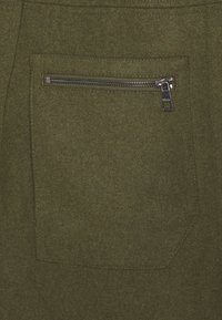 Oliiviv roheline kangas tasku, mille ülemisel küljel on horisontaalne hõbedane tõmblukk, õmmeldud vastava tekstuuriga materjalile.