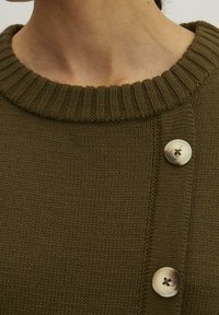 Dzianinowy sweter w oliwkowym kolorze z żeberkowym kołnierzykiem i trzema guzikami po lewej stronie; cechuje się teksturowanym wykończeniem i dopasowanym krojem.