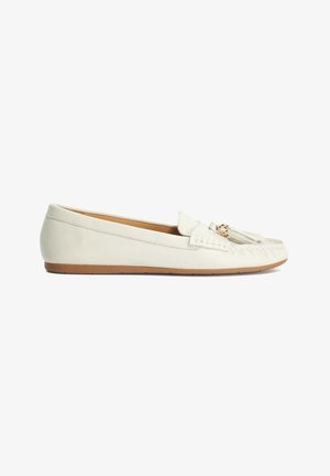 Mocassin plat en cuir blanc avec pompons et accent doré sur une semelle marron clair, présenté de profil sur un fond blanc.