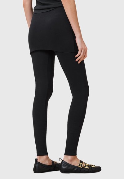 Leggings noirs et jupe noire, en tissu extensible. La tenue est assortie à des ballerines noires avec des accents en métal doré.