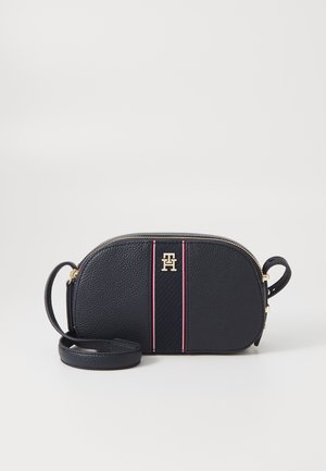 Sac bandoulière bleu marine avec logo TH doré, rayures verticales rouges et blanches, fermeture zippée et sangle ajustable sur fond blanc uni.