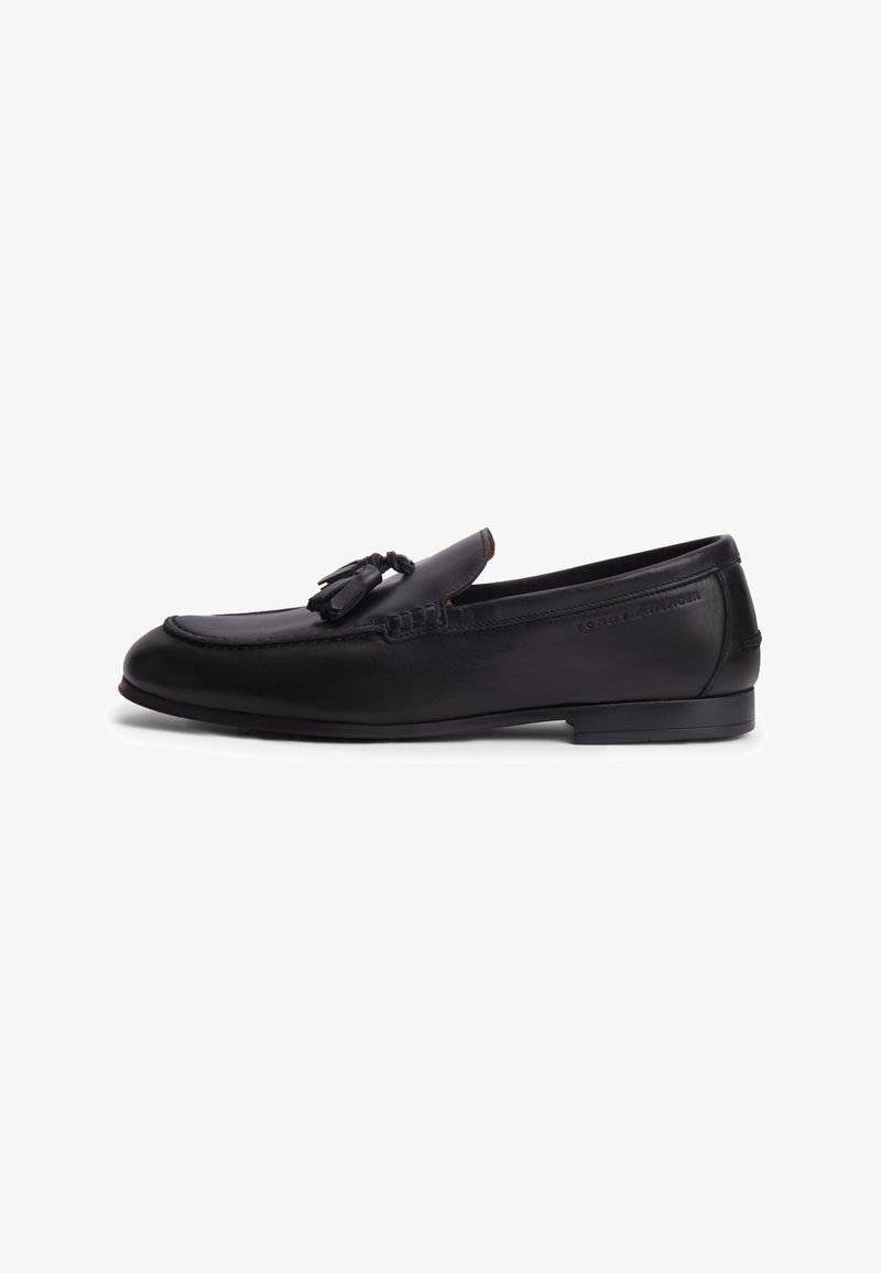 Μαύρο δερμάτινο loafer με φούντες, χαμηλό τακούνι και ραμμένα στοιχεία σε λευκό φόντο.