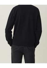 Schwarzer Sweatshirt mit langen Ärmeln, geripptem Saum und Bündchen. Der Stoff wirkt weich und strukturiert. Gesehen von hinten, kombiniert mit grauer Hose.