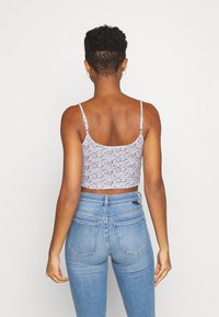 Ljuslila cropped tanktop med blommönster, tunna axelremmar, i kombination med högmidjade blå denimjeans. Mjuk tyg och figursydd design.