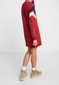 Robes de sport rouge avec des manches bloc de couleurs en marine, beige et crème. Texture douce, col rond et coupe décontractée. Associée à des bottes épaisses beiges.