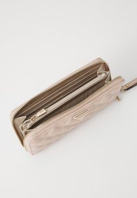Portafoglio beige trapuntato con chiusura a zip, dotato di più scomparti e un accento metallico. Texture liscia e hardware in tonalità oro sono visibili.