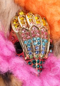 Gouden ring met meerdere kleurrijke edelstenen, waaronder roze, blauw en groen, in een gestructureerd ontwerp, met een fluffy roze en oranje achtergrond.