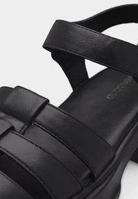 Μαύρο δερμάτινο σανδάλι με φαρδιές λουρίδες και τετράγωνο τακούνι, με επενδυμένο πέλμα και λουρί στήριξης αστραγάλου.