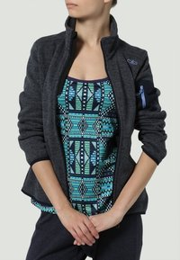 Giacca in pile nera con zip, canotta a righe blu navy e teal sotto. Maniche lunghe con dettagli blu e tessuto testurizzato.