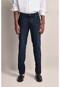 Ciemnoniebieskie dżinsy o prostym kroju, z pięcioma kieszeniami, subtelnymi detalami przeszycia i gładkim wykończeniem, w połączeniu z czarnymi butami.