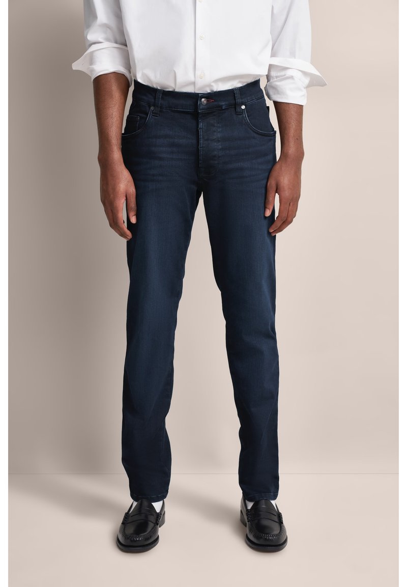 Ciemnoniebieskie dżinsy o prostym kroju, z pięcioma kieszeniami, subtelnymi detalami przeszycia i gładkim wykończeniem, w połączeniu z czarnymi butami.