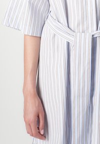 Manga curta, vestido riscado azul e branco com um formato em A, apresentando um cinto na cintura e riscas verticais texturizadas em castanho.