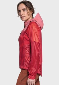 Rote technische Jacke mit einer pinken Kapuze, die durch ein elegantes Design, leichtes Material und eine Seitenasche besticht. Sanfte Textur, wasserabweisende Oberfläche.