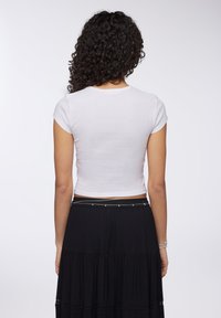 Top corto a maniche corte, bianco e a costine, abbinato a una gonna nera a strati con una cintura decorativa e sottili dettagli in pizzo.