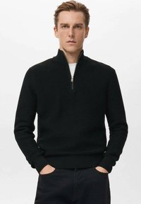 Czarny sweter z suwakiem sięgającym do ćwiartki, z teksturowanym wzorem dzianiny, ściągaczami na mankietach i u dołu. Noszony na białym t-shircie, z metalowym suwakiem jako detalem.