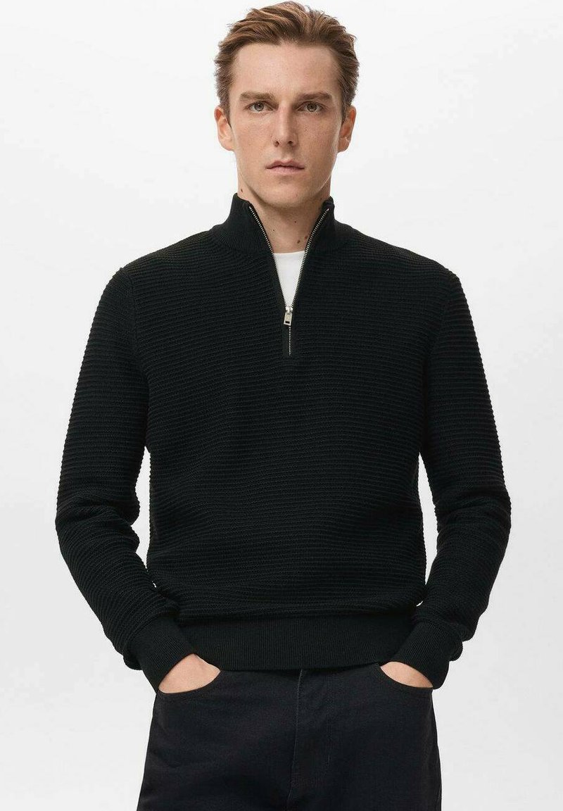 Czarny sweter z suwakiem sięgającym do ćwiartki, z teksturowanym wzorem dzianiny, ściągaczami na mankietach i u dołu. Noszony na białym t-shircie, z metalowym suwakiem jako detalem.