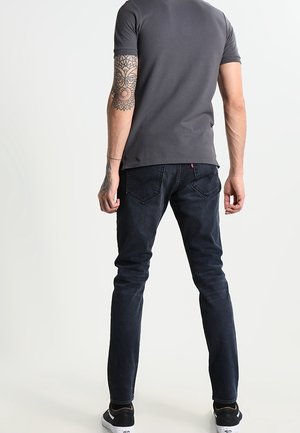 Dark blue jeans with a slim fit, paired with a dark gray short-sleeve t-shirt. Features visible stitching and a subtle design on the t-shirt.