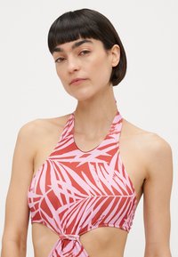 Rood en roze halterbikini-top met palmbladpatroon, uitsnijdingen aan de zijkanten en knoopdetail aan de voorkant. Gemaakt van rekbare, soepele stof.