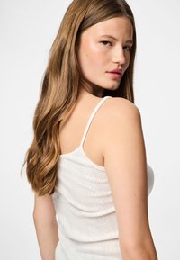 Top bianco senza maniche con una texture a coste e sottili righe verticali. Presenta spalline sottili e un design aderente.