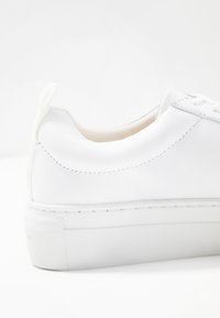 Hvite sneakers laget av glatt lærmateriale, med avrundet form og tykk gummisåle med diskret søm og minimal merking.