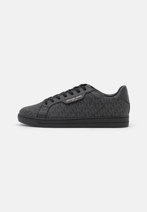 Black sneakers featuring a textured fabric upper with a subtle MK pattern, black leather accents, and a black rubber sole.