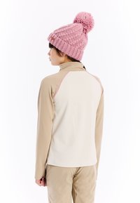 Langarmtop in beige met roze accenten, gemaakt van glad, rekbaar materiaal; gecombineerd met een chunky roze gebreide muts met een pompon.
