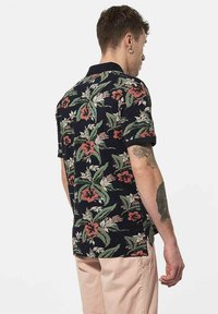 Korte mouwen zwart shirt met een kleurrijk bloemenpatroon met rode en groene accenten. Gemaakt van een lichtgewicht materiaal.