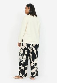 Maglione crema a maniche lunghe, abbinato a pantaloni palazzo neri e bianchi con stampa floreale e ballerine rosa chiaro.
