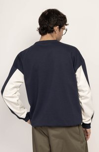 Navy blue sweatshirt with white sleeves, crew neck, and relaxed fit. Soft fabric with contrasting color-block design on sleeves.