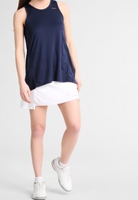 Marinblå atletisk linne med rund halsringning och lös passform, kombinerat med en vit tennis minikjol; har subtil logotyp på linnet.